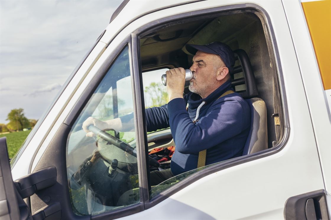 A person drinking from a can in a truck

Description automatically generated